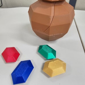 May include: Four 3D printed gems in red, green, blue, and yellow. The gems are sitting on a white surface next to a brown, cracked, 3D printed vase.