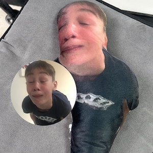 Peut inclure: Un oreiller personnalisé avec le visage d'une personne. L'oreiller est fait d'un tissu doux et porte un t-shirt noir avec le texte "LAFAY" imprimé dessus.