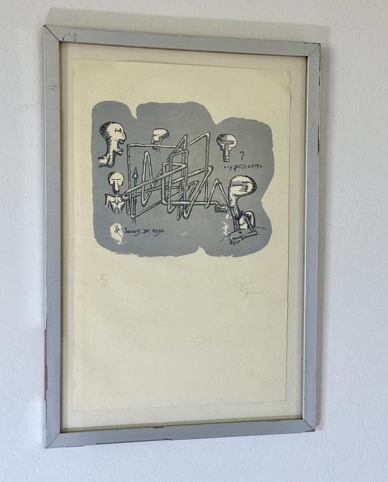 K&ouml;nnte beinhalten: Ein gerahmter Druck mit einer grauen zentralen Form, die schwarze Strichzeichnungen stilisierter Figuren und eine komplexe rohrartige Struktur enth&auml;lt. Der Text lautet "Juegos de mesa" und "...y de dentro". Der Druck ist mit 8/18 nummeriert und signiert.