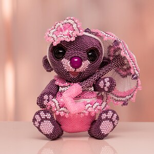 Beaded purple teddy bear in a pink dress with lace panties and a cute headband holding a white and pink umbrella. Handmade figurine created with peyote stitch, front view.