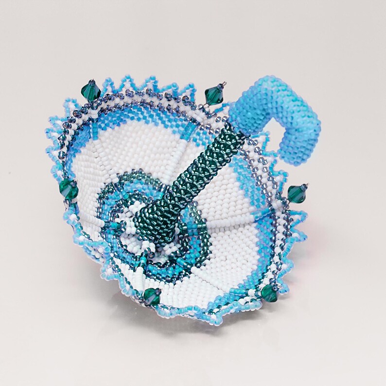 White and light blue beaded umbrella rests upside down on its dome. Peyote stitch miniature accessory pattern.
