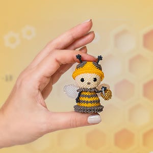 A girl gently holds a tiny beaded bee wearing a yellow hat and carrying a golden honey bucket, showcasing the miniature insect created with a Peyote Stitch pattern.