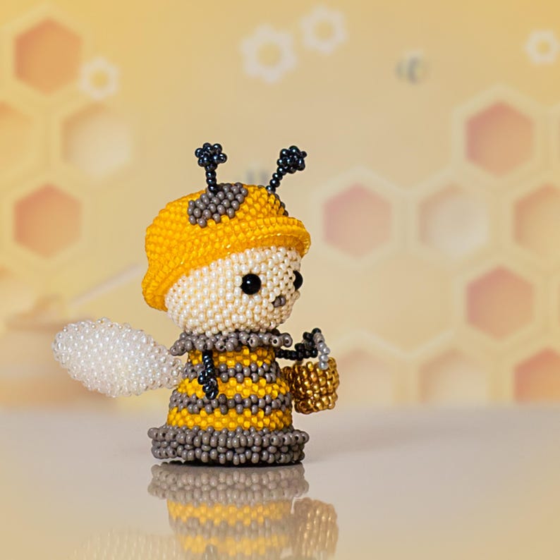 Cute beaded bee wearing a yellow hat and lifting one hand while turning right, holding a tiny golden honey pail; ideal for a beaded figurine tutorial.