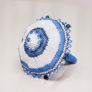 White and blue beaded umbrella in peyote stitch lying with the dome facing forward on its spokes. Detailed beadwork pattern.