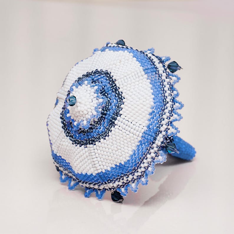 White and blue beaded umbrella in peyote stitch lying with the dome facing forward on its spokes. Detailed beadwork pattern.