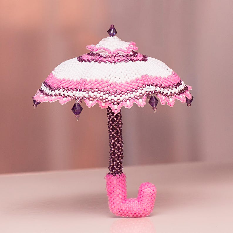 White and pink beaded umbrella made using peyote stitch stands upright on its handle. Elegant handmade miniature.