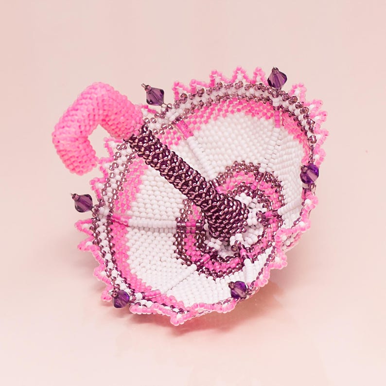 White and pink beaded umbrella made in peyote stitch rests upside down on its dome with the handle facing upward.