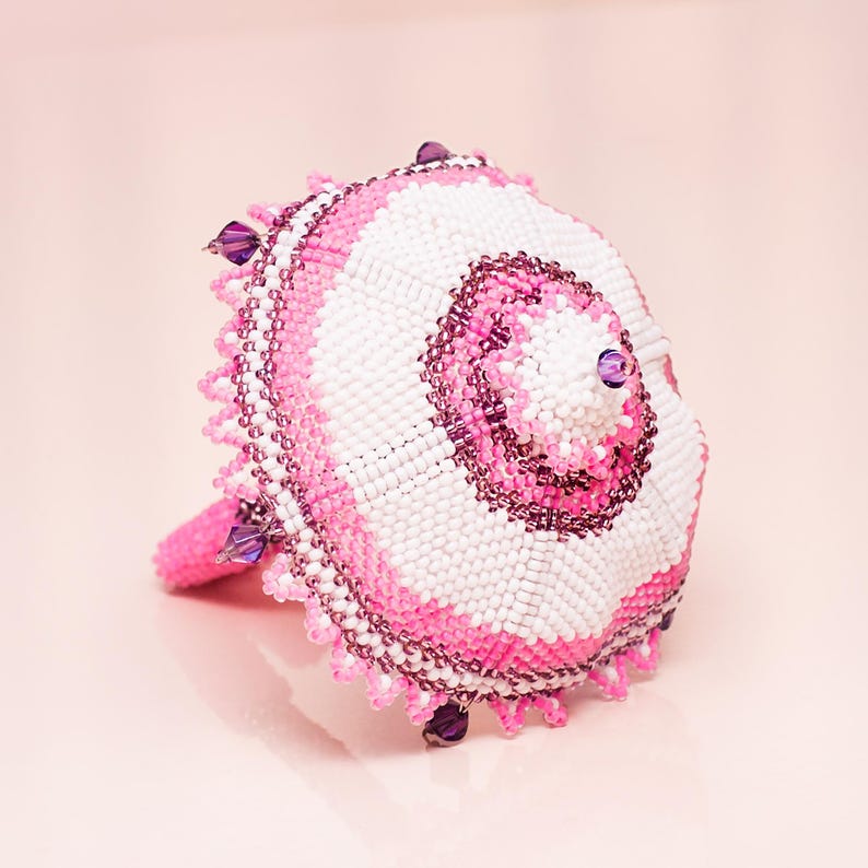White and pink peyote stitch umbrella lying on its spokes with the dome facing forward. Delicate seed bead pattern.