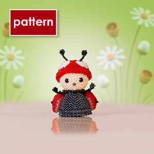 Puede incluir: Una figura de mariquita de cuentas con gorro rojo y blanco, cuerpo negro y alas rojas. La palabra "pattern" está en un cuadro rojo en la esquina superior izquierda. El fondo es verde suave con flores blancas.