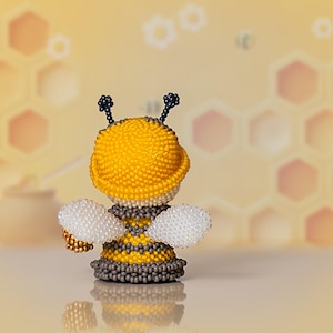 Back view of a cartoon-style beaded bee in a yellow hat holding a golden honey bucket, highlighting shape and beadwork texture for the bee pattern.