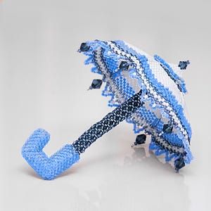 Side view of a white and blue umbrella made of seed beads in peyote stitch lying on its spokes.