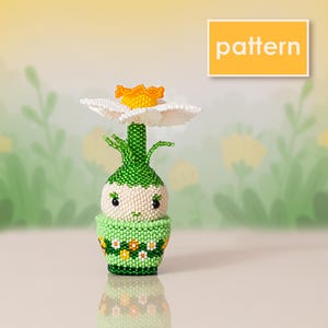 May include: A beaded figurine of a small character with a round cream-colored face and black eyes, wearing a green pot decorated with white and yellow flowers. A green stem rises from the head, topped with a white and yellow flower. Text reads pattern.