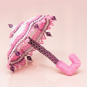 Side view of a white and pink umbrella made from seed beads in peyote stitch, lying on its spokes.