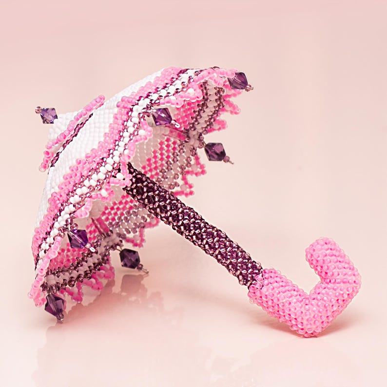 Side view of a white and pink umbrella made from seed beads in peyote stitch, lying on its spokes.