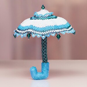 White and light blue umbrella crafted from seed beads in peyote stitch stands upright on its handle. Handmade miniature beadwork.