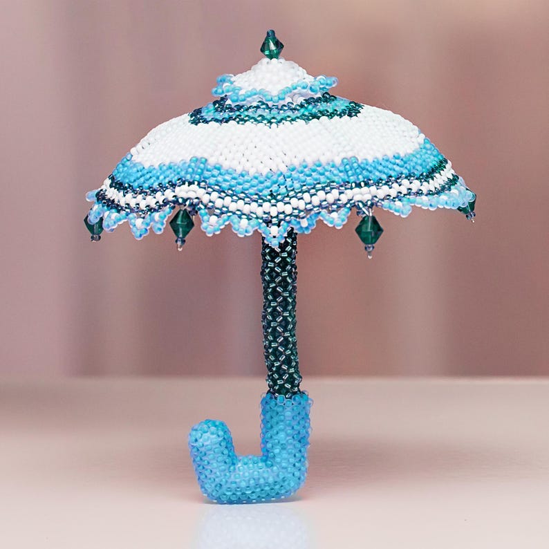 White and light blue umbrella crafted from seed beads in peyote stitch stands upright on its handle. Handmade miniature beadwork.