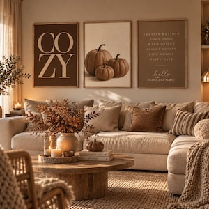 K&ouml;nnte beinhalten: Drei rechteckige Wandbilder in Holzrahmen h&auml;ngen &uuml;ber einem Sofa. Das linke Bild zeigt das Wort COZY in gro&szlig;en Buchstaben. Das mittlere Bild zeigt drei braune K&uuml;rbisse. Das rechte Bild listet herbstliche Phrasen und den Text hello autumn auf.