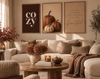 Könnte beinhalten: Drei gerahmte Wandbilder, bestehend aus einem dunkelbraunen Poster mit dem Wort cozy, einem zentralen Druck mit drei Kürbissen und einem hellbraunen Poster mit dem Text Autumn is proof that change can be beautiful, über einem beigen Sofa.