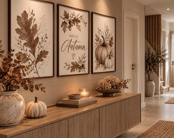 Könnte beinhalten: Ein Set aus drei gerahmten Wandbildern mit braunen botanischen Illustrationen von Eichenblättern, Eicheln und Kürbissen, inklusive dem Text "HELLO Autumn" und einem Herzsymbol, platziert über einem hölzernen Konsolentisch.
