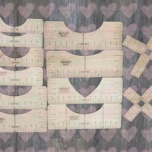 May include: A selection of wooden garment templates for different sizes, including infant, toddler, youth, and adult. Each template has measurement markings and labels such as "FRONT," "BACK," and "POCKET." Two cross-shaped templates are also present.