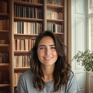 Könnte beinhalten: Eine Frau mit langen braunen Haaren lächelt in die Kamera. Sie steht vor einem Bücherregal, das mit Büchern gefüllt ist. Das Bücherregal ist aus Holz und hat eine hellbraune Oberfläche. Die Frau trägt ein graues Shirt.