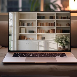 May include: A silver laptop computer with a white keyboard and trackpad is open on a light brown couch. The laptop screen shows a white bookshelf filled with books.