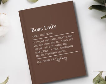 May include: A brown notebook with the text "Boss Lady (BOS-LADE) NOUN. A strong and intelligent woman who can complete all tasks set before her with grace and confidence; a true superhuman and multitasking expert. ALSO KNOWN AS: Sydney" printed in white.