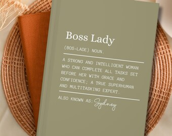 May include: A green journal with the text "Boss Lady (BOS-LADE) NOUN." and a definition of the term. The text "ALSO KNOWN AS: Sydney" is written in cursive at the bottom of the page.