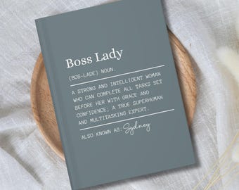 May include: A gray notebook with the text "Boss Lady (BOS-LADE) NOUN. A strong and intelligent woman who can complete all tasks set before her with grace and confidence; a true superhuman and multitasking expert. ALSO KNOWN AS: Sydney" printed in white.