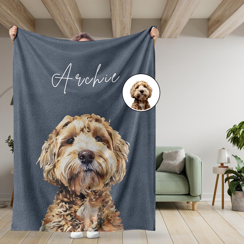 May include: A gray fleece blanket with a personalized name "Archie" in white cursive script. A brown and white dog's face is printed on the blanket, with a smaller image of the dog's face in a circle in the upper right corner.