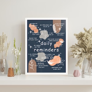 May include: A framed print with a navy blue background and white text that reads "daily reminders." The print includes inspirational phrases in white, peach, and gray, such as "Celebrate Every Damn Win" and "Empower Your Damn Self."