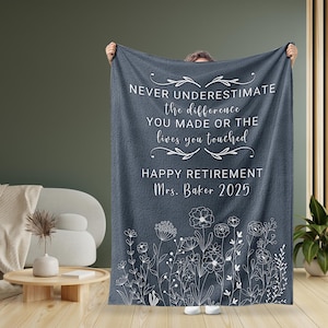 May include: A gray fleece blanket with white text that reads "Never underestimate the difference you made or the lives you touched. Happy Retirement Mrs. Baker 2025". The blanket has a white floral design at the bottom.
