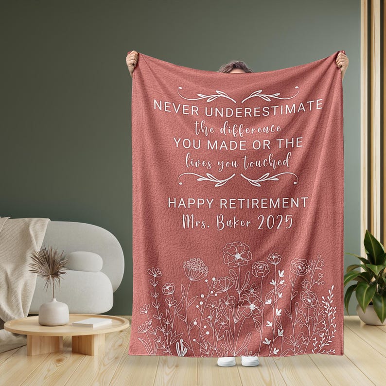 May include: A pink fleece blanket with a white floral design and the text "NEVER UNDERESTIMATE the difference YOU MADE OR THE lives you touched HAPPY RETIREMENT Mrs. Baker 2025".