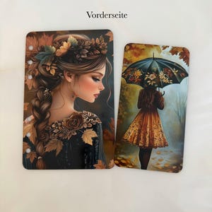 Könnte beinhalten: Zwei rechteckige Karten mit herbstlichen Illustrationen. Eine zeigt eine Frau mit Blumenkranz und Blättern, die andere eine Person mit einem Regenschirm in einem Wald. Der Text "Vorderseite" steht oben.