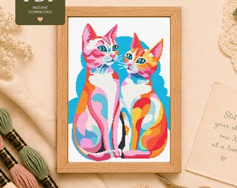 May include: A cross stitch pattern featuring two cats in vibrant shades of pink, orange, blue, and white, set against a bright blue background. The cats are depicted in a stylised, colourful manner within a light wooden frame, presented as a PDF.