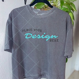 May include: A gray t-shirt with a black hanger. The shirt has the text "Place Your Design Here" in a blue and pink font.