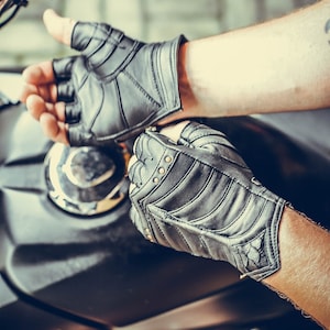 May include: A pair of black leather fingerless gloves with a zipper detail and decorative stitching. The gloves have a textured surface and are worn by a person.