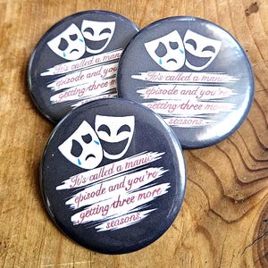May include: Three dark grey round badges with a theatre mask design. Each badge features a smiling and a crying mask, with the text "It's called a manic episode and you're getting three more seasons."