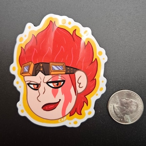 May include: A sticker featuring a cartoon character with red hair, goggles, and a determined expression. The character has a flame-like design on their face and is surrounded by a yellow border. The sticker is next to a U.S. quarter for size comparison.