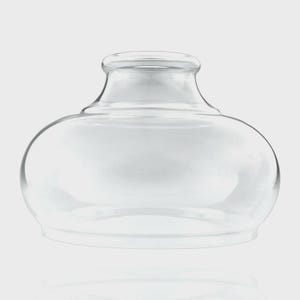 Pode incluir: Um abajur de vidro transparente com um corpo arredondado e bojudo, e uma abertura cilíndrica mais estreita no topo. O vidro é liso e transparente, apresentando uma ampla abertura circular na base para fixação em um suporte de luz.