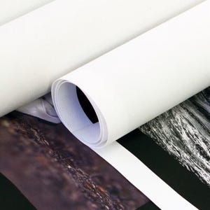 May include: A close-up of a white canvas print rolled up. The print is on a black surface with a black and white image of water.
