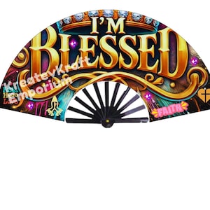 May include: A black folding fan with a colorful design featuring the words "I'm Blessed" in gold lettering. The fan has a gold and black crown, a pink ribbon with the word "Faith", and other decorative elements.
