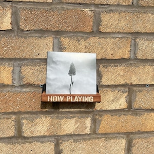 May include: A wooden shelf with the words "NOW PLAYING" printed on it. A black and white photograph of a tree and a person is displayed on the shelf.