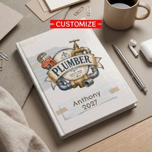 May include: A white hardcover notebook featuring a graphic of a pipe wrench and plumbing fixtures surrounding a banner with the text PLUMBER, QUALITY WORK BUILT TO LAST, and the name Anthony 2027 printed in a rectangular box on the lower cover.