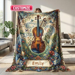 Puede incluir: Una manta rectangular con una ilustración central de un violín rodeada de notas musicales, coloridos motivos florales y árboles. El diseño incluye una banda en la parte inferior con el nombre Emily y una etiqueta roja que dice CUSTOMIZE.