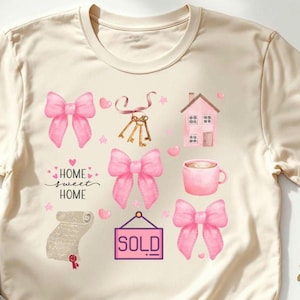 May include: Cream-colored t-shirt featuring a watercolor design of pink bows, keys, a house, a coffee cup, and a scroll. The text "HOME sweet HOME" is also included. A "SOLD" sign is also present. The design has a real estate theme.