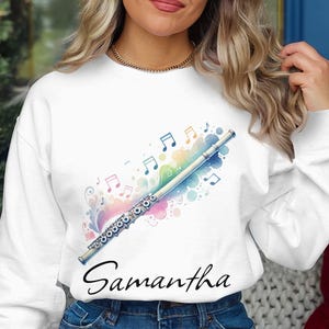 May include: White sweatshirt with a watercolor design of a flute and musical notes. The text "Samantha" is printed below the design.