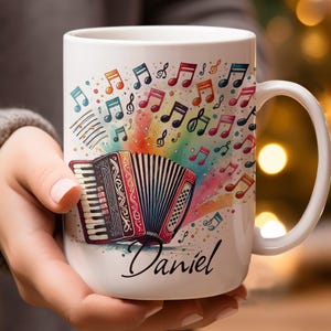 May include: White ceramic mug with a colorful illustration of an accordion and musical notes. The mug has a handle and the name "Daniel" is printed on the bottom.