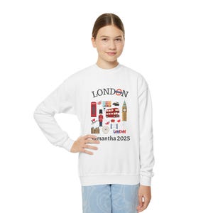 May include: White sweatshirt with a London themed design. The design includes a red double-decker bus, Big Ben, a red telephone booth, and the Union Jack flag. The text "LONDON" is printed in black at the top of the design. The text "Samantha 2025" is printed in black at the bottom of the design.