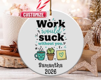 May include: A white ceramic Christmas ornament with the text "Work would suck without you." and a personalized name and year. The design includes a coffee cup, cactus, and sticky note. A gold string is attached for hanging.